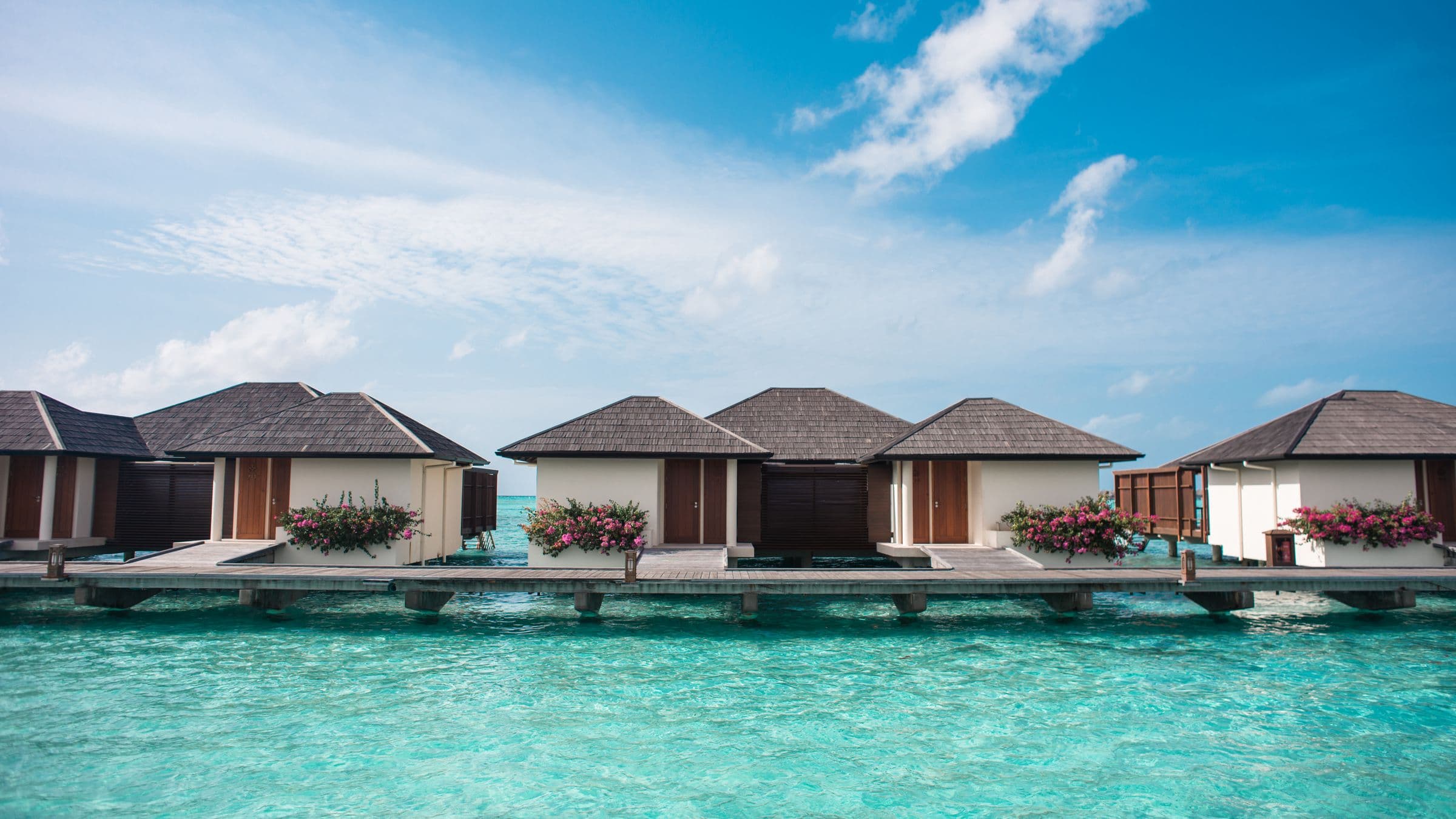 Overwater villas above turquoise water under a wide blue sky, Maldives